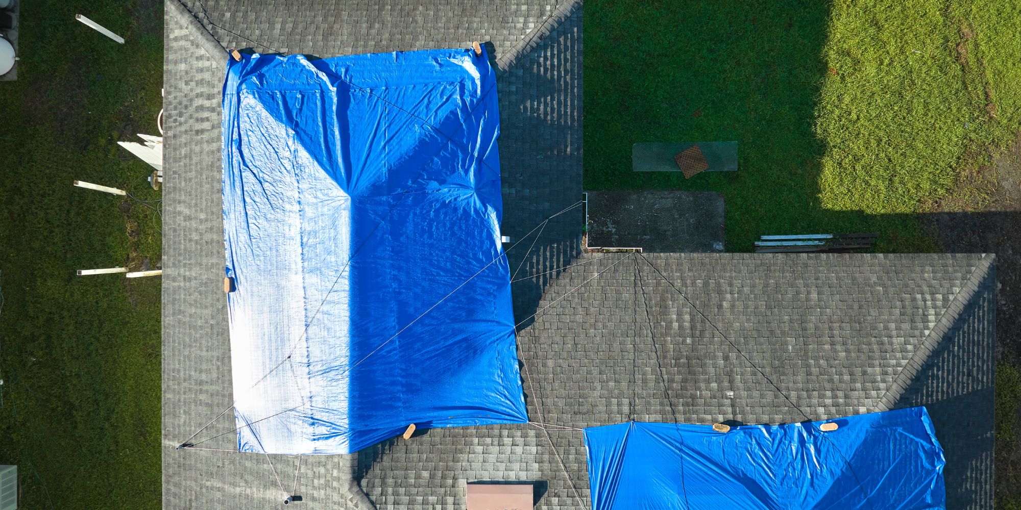 Exemple de bâchage de toiture vu du ciel : des bâches bleues recouvrent le faîtage et de chaque côté une partie du toit incliné