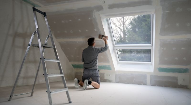 Homme platrant des cloisons seches dans une piece mansardee