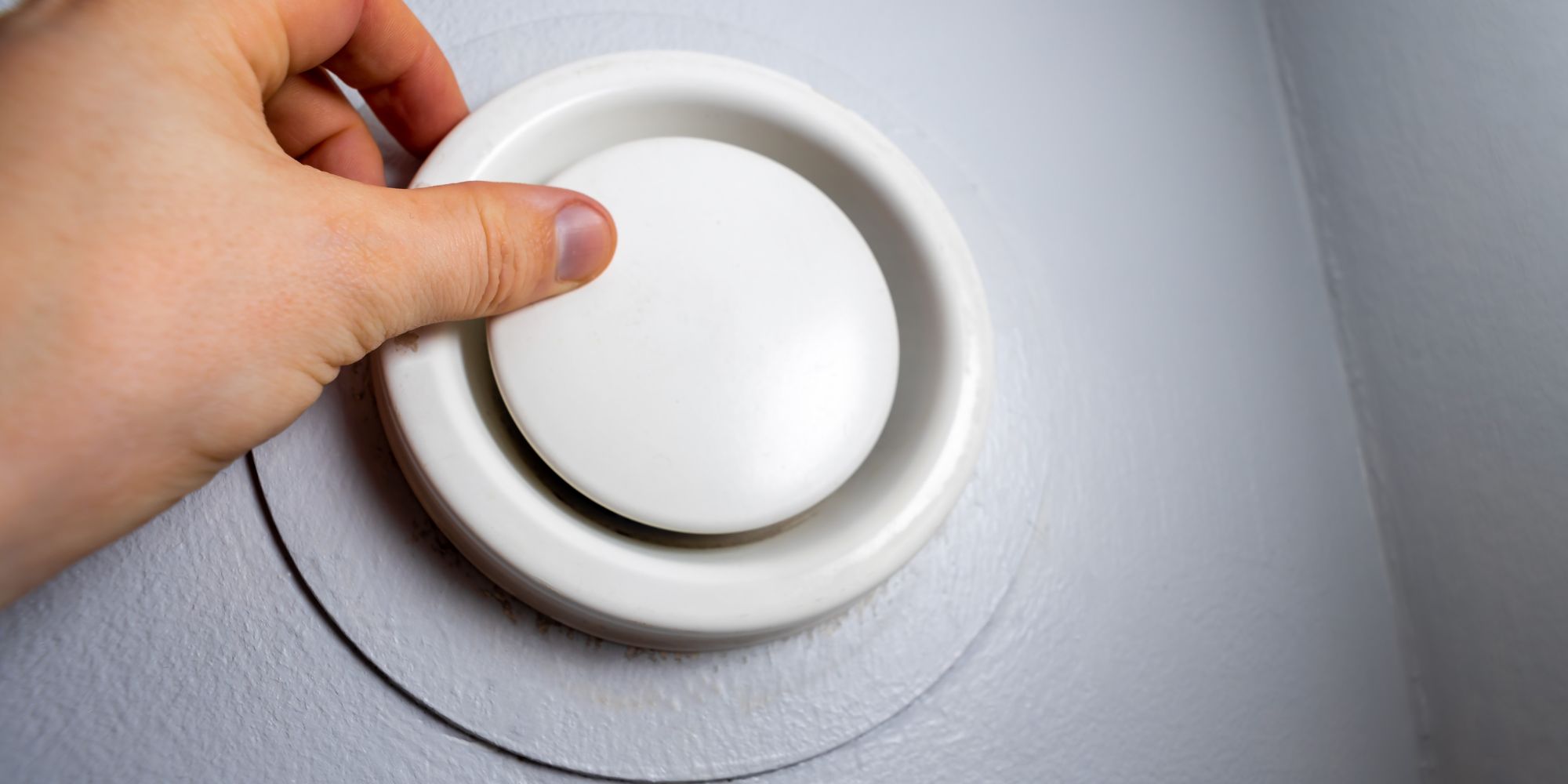 Main s'apprêtant à retirer le capôt d'une bouche d'extraction, pour illustrer l'idée de l'entretien de la VMC