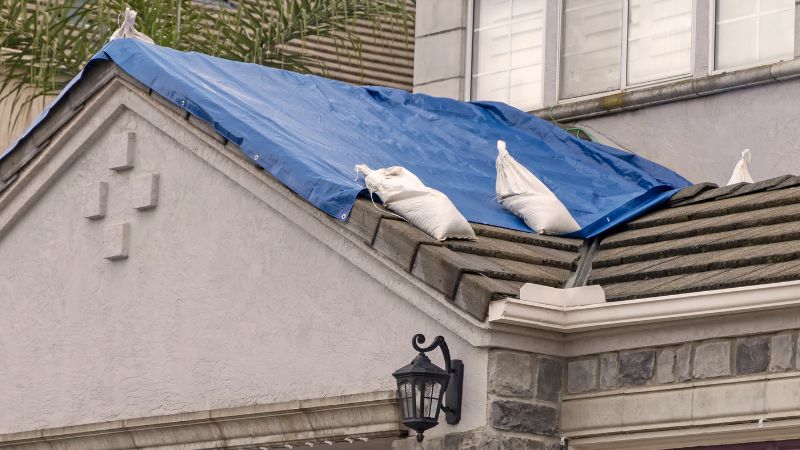 Bâche bleue installée sur une toiture en pente avec des sacs de sable, parfois nécessaires pour bâcher un toit sans percer.
