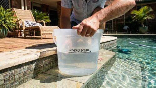 seau d'eau immergé, posé sur la marche d'une piscine pour détecter une fuite