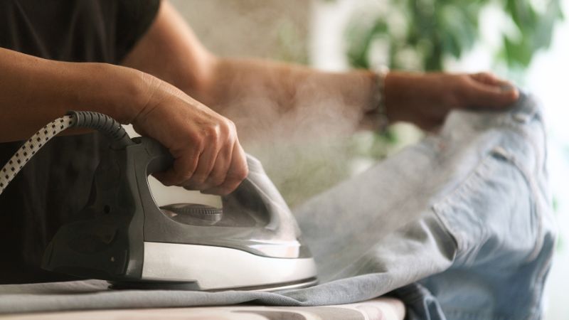 Personne repassant un vêtement à la vapeur chaude – geste préventif utile pour éviter les punaises de lit chez soi