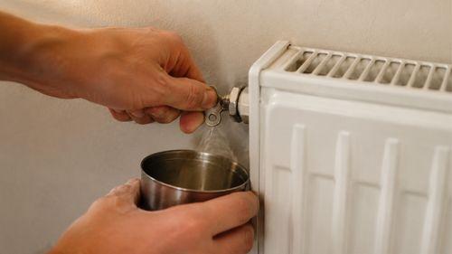 Main ouvrant le purgeur d'un radiateur avec une clé de purge