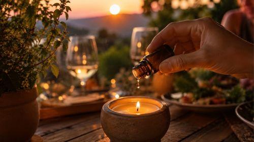 Ajout de quelques gouttes d'huile essentielle dans une bougie allumée sur une table de terrasse au crépuscule pour éloigner les guêpes de la table