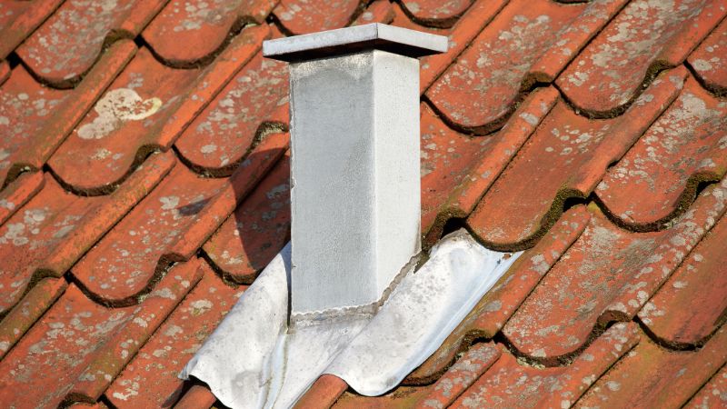 Solin métallique à la base d’une cheminée sur un toit en tuiles anciennes, zone à risque de fuite toiture par forte pluie.