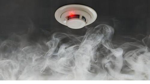 détecteur de fumée installée au plafond avec fumée et voyant rouge