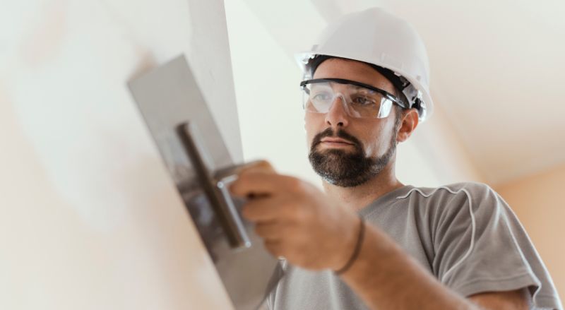 professionnel en train de lisser un enduit sur un mur avec une lame en inox
