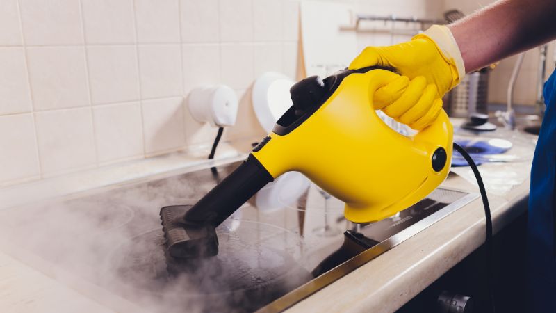 Personne qui utilise un nettoyeur vapeur sur une plaque de cuisson