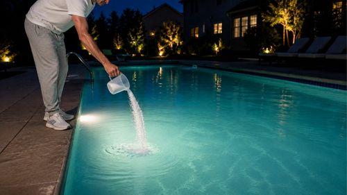 Versement de chlore choc dans une piscine au bord du bassin la nuit pour traiter une eau trouble blanche