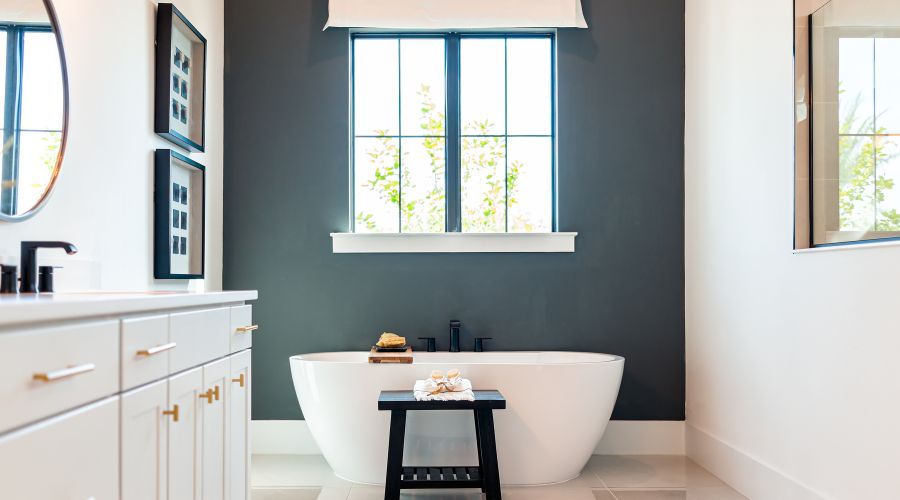 salle de bain en longueur avec dans le fond un mur peint en vert fonce une fenetre une baignoire a droite un grand miroir a gauche le meuble vasque et deux cadres l un au dessus de l autre