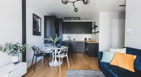 exemple de studio de 30 m2 bien amenage avec canape convertible en velours bleu cuisine noire table a manger ronde laquee blanche petit meuble tv blanc en acier parquet et luminaire boules design