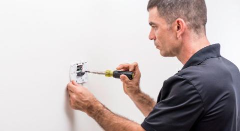 electricien en train de proceder au branchement d un thermostat 2 ou 3 fils et a la fixation du boitier sur le mur
