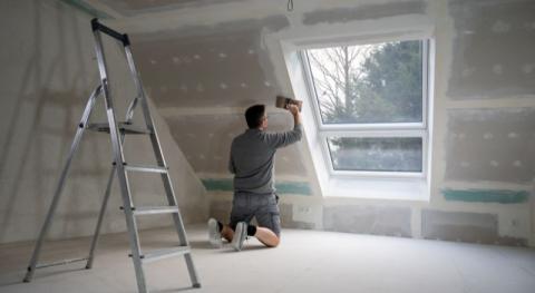 Homme platrant des cloisons seches dans une piece mansardee