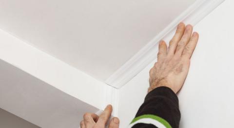 homme en train de coller une moulure fine et plate dans un angle de plafond 