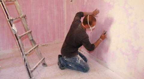 un professionnel equipe d un masque en train de poncer un mur avec une cale a poncer