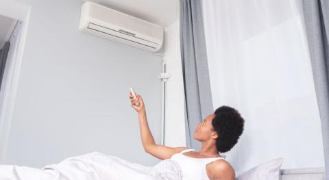 femme allongee dans son lit reglant son climatiseur mural 