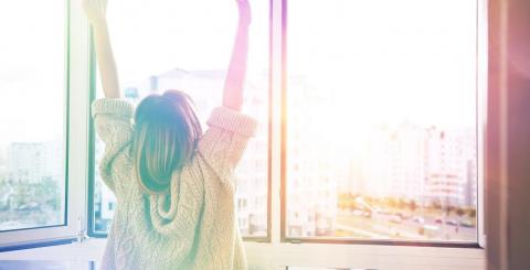 Jeune femme devant sa fenêtre et des rayons de soleil.