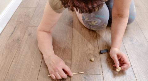 une femme agenouillee au sol en train de reparer son parquet endommage